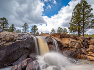 a small waterfall flowing over jagged rust-colored rocks